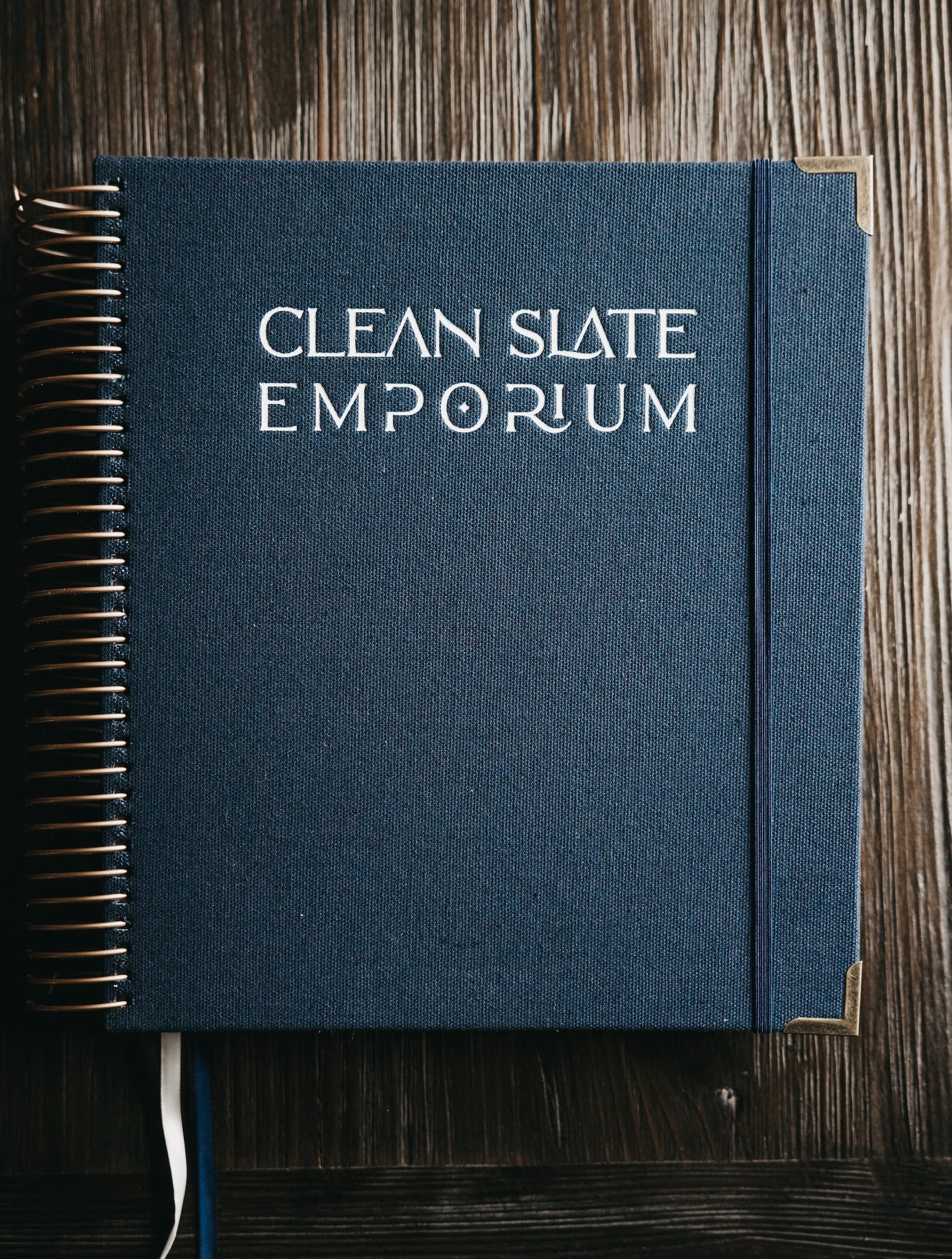 Blue notebook with 'Clean Slate Emporium' embossed on the cover, placed on a wooden surface.