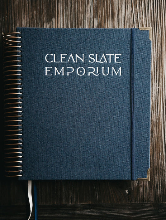 Blue notebook with 'Clean Slate Emporium' embossed on the cover, placed on a wooden surface.